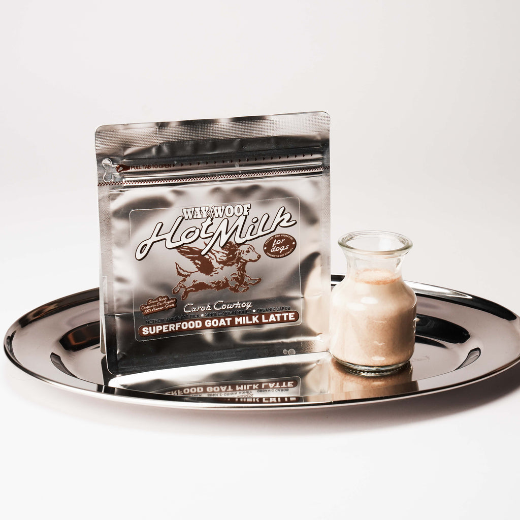 Foil bag of "Hot Milk" powder blend on a plate with a small glass bottle of the product mixed with water.