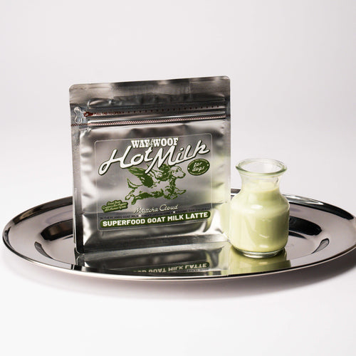 Foil bag of "Hot Milk" powder blend on a plate with a small glass bottle of the product mixed with water.